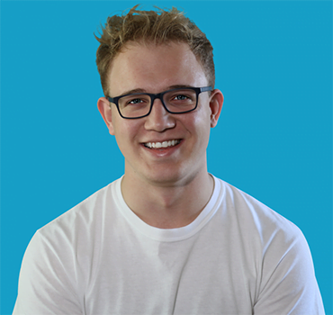 Jack Dryden • Fringe Theatre Producer | Profile picture of Jack Dryden, head and shoulders picture of Jack who has blond hair and square navy glasses, against a teal blue background.